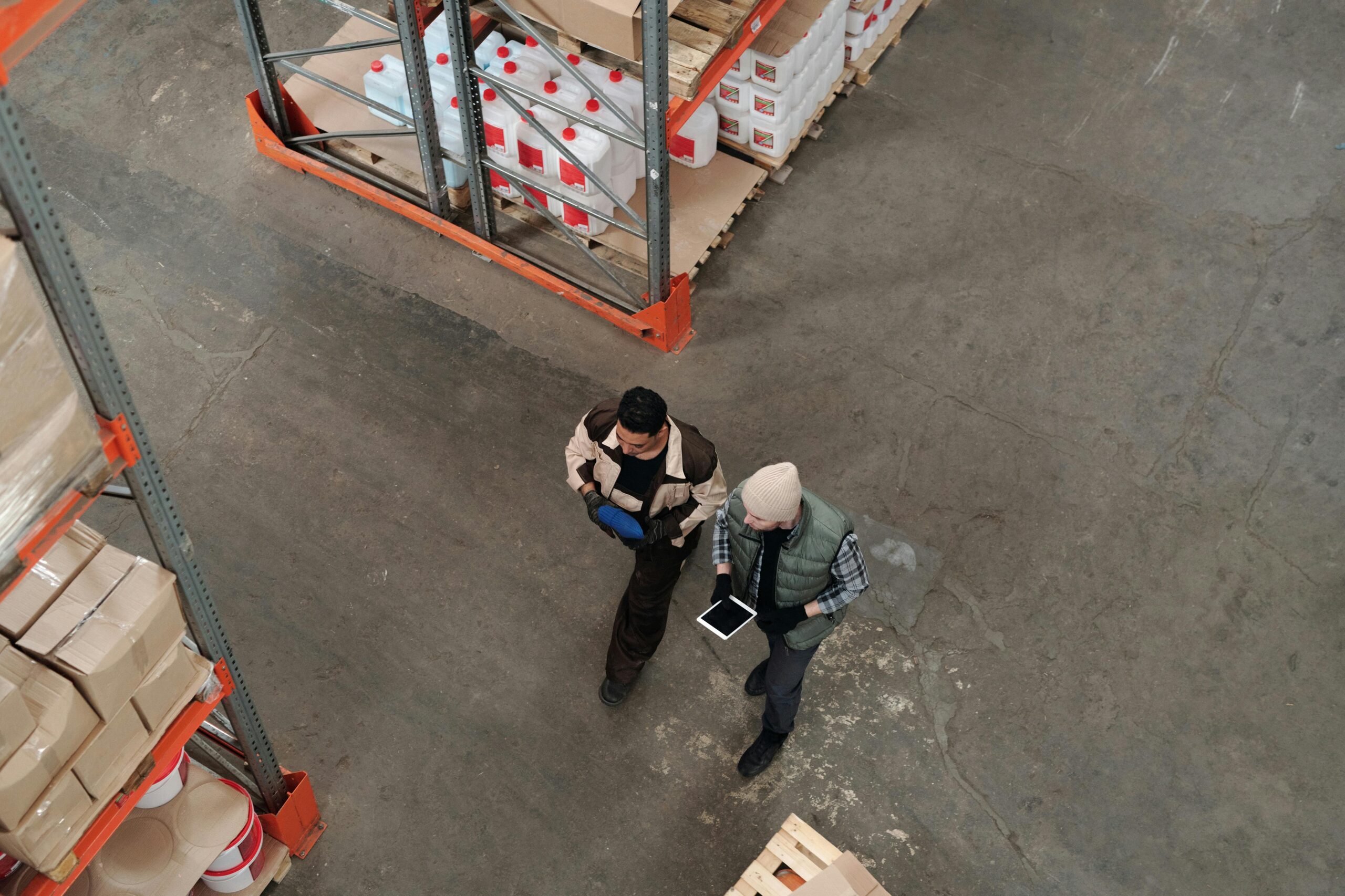 Two workers discussing inventory in a warehouse, using a digital tablet for coordination.