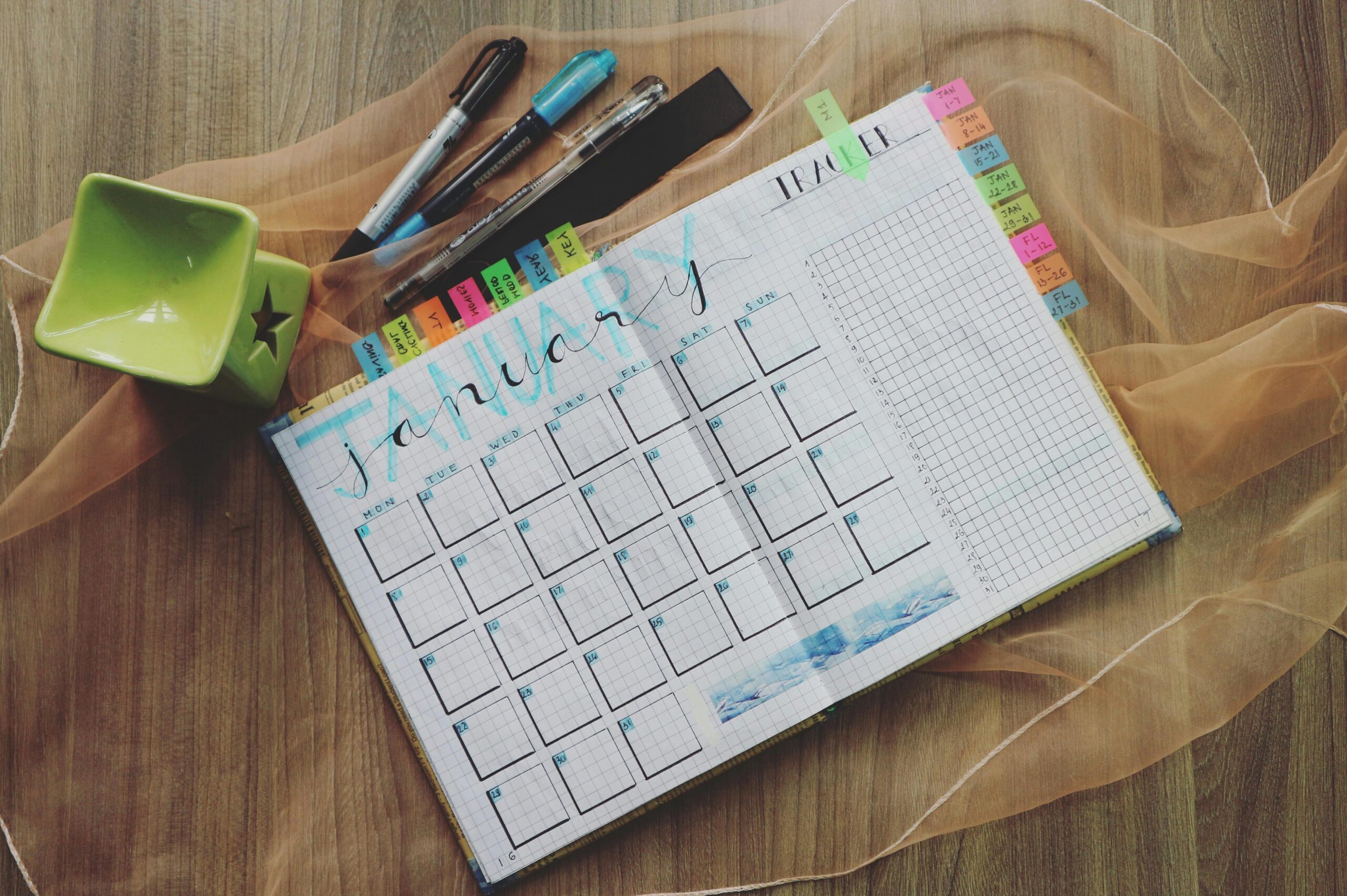 Top view of a January planner with pens and a green cup, ideal for organizing tasks.